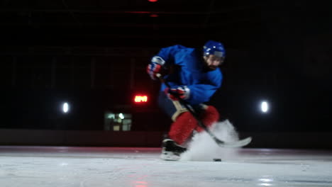 Nahaufnahme-Des-Pucks-Auf-Dem-Eis-Und-In-Zeitlupe-Fährt-Der-Eishockeyspieler-Hoch,-Der-Schnee-Fliegt-In-Die-Kamera-Und-Er-Nimmt-Den-Puckschläger